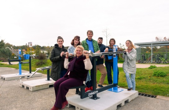 Zes volwassenen demonstreren samen een buitensporttoestel in een park. (vergroot foto)