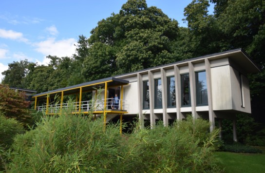 Woonzorgcentrum De Ceder: Modern huis met gele balustrade, omgeven door bomen en siergrassen. (vergroot foto)