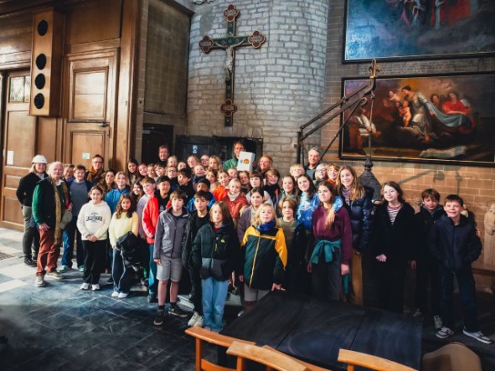 Groep kinderen en volwassenen poseren in de kerk van Alsemberg met kruis en schilderijen aan de muur. (vergroot foto)