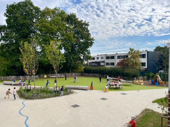 Kinderen spelen op de speelplaats van GBS Blokbos met grasveld, picknicktafels en speeltoestellen onder een mooi bewolkte lucht. (vergroot foto)