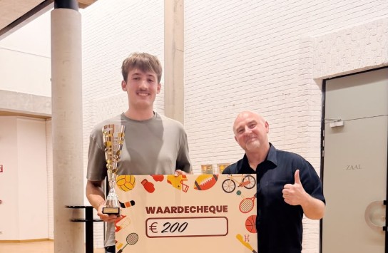 Twee mannen poseren met een trofee en een waardebon van €200 in een zaal met houten vloer. (vergroot foto)